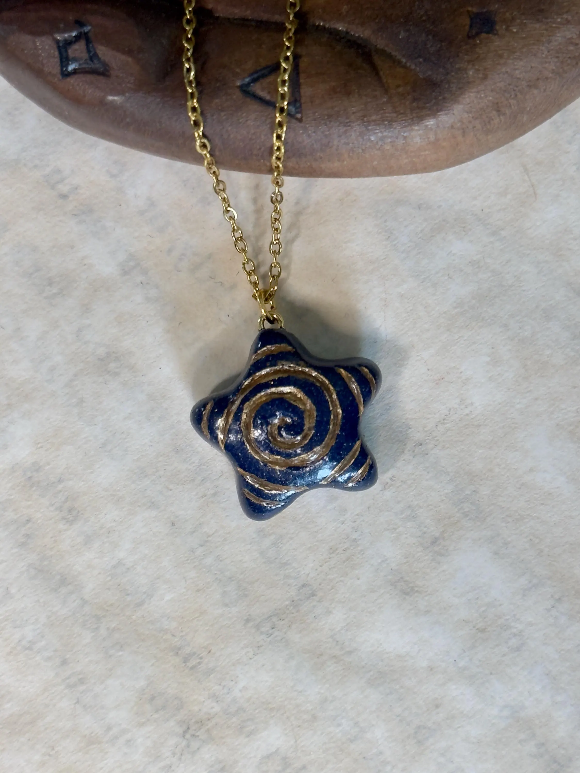 Star-shaped pendant with gold spiral design on a gold chain, displayed against a neutral background.