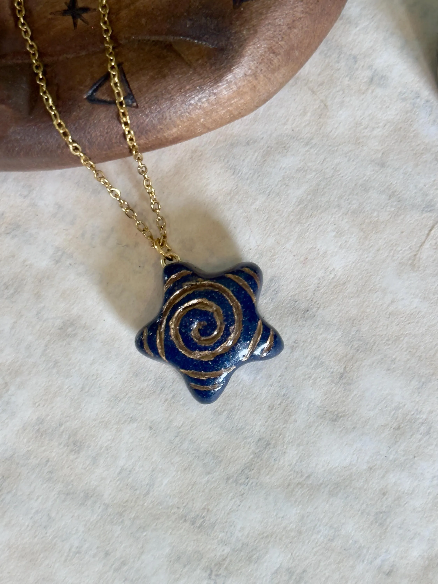 Blue spiral pendant necklace on a gold chain against a neutral background