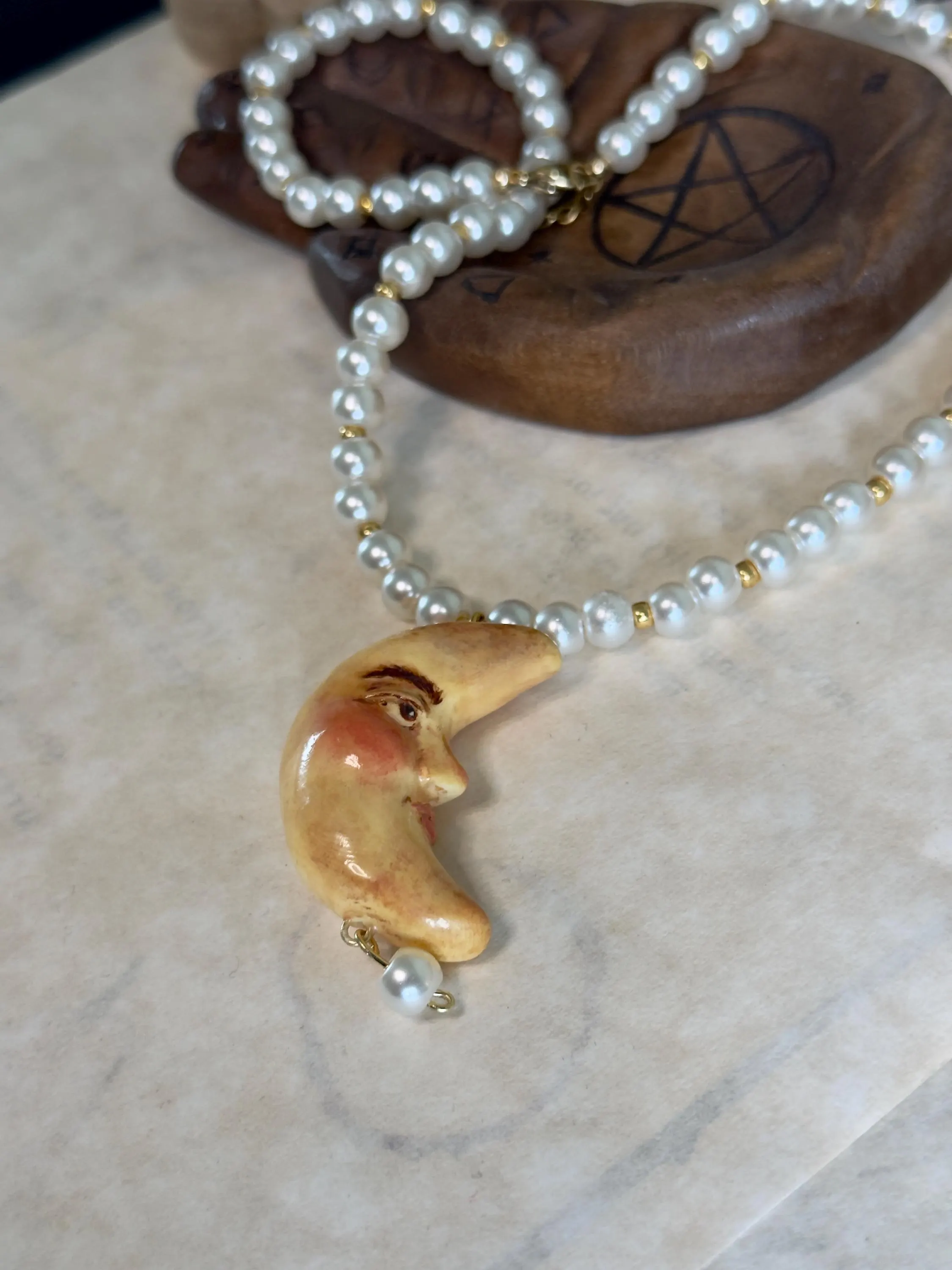 Pearl necklace with a handmade, vintage moon pendant on a marble surface. Witchy, whimsical jewellery